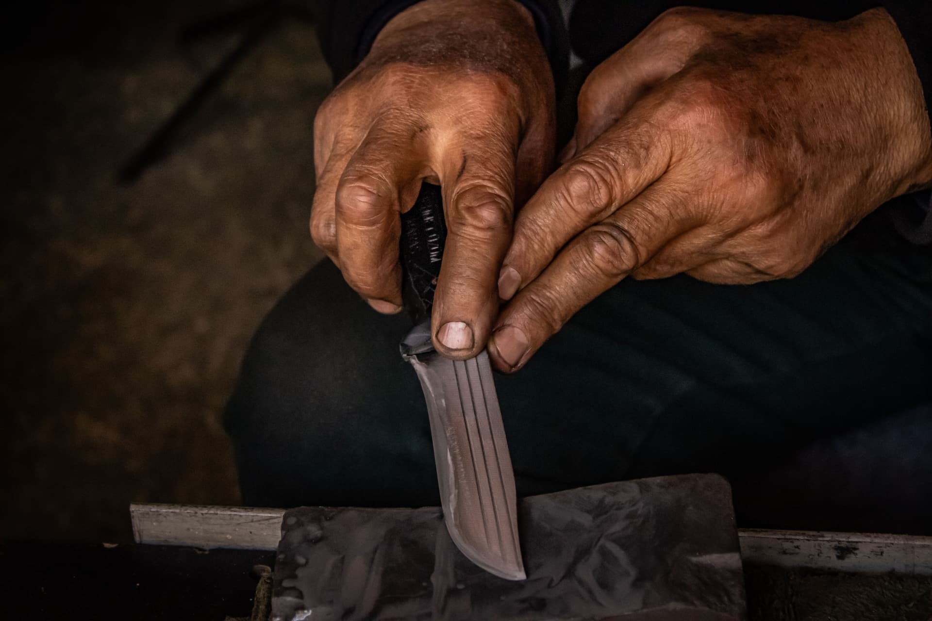 Hands drawing a knife across a wet whetstone
